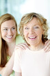 © ReeseBuyout4/peopleimages.com - Portrait, mature mother and daughter in home with bonding, smile and morning embrace in living room together. Relax, senior mom and girl with happy face for love, care and family support in apartment