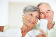 © STEEXBuyout/peopleimages.com - Home, senior couple and music with earphones for listening, hearing and connection for bonding together. Living room, man and woman in retirement with mp3 player, blues and classic pop for relaxation