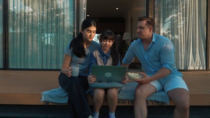 Father, mother and daughter focus laptop at terrace with garden view outside house. Parent use outdoor activity to communicate young generation about environment care cross generation gap. Divergence.