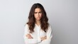 © Iona - A young woman in a white blouse crosses her arms and eyes the viewer with a displeased and doubtful expression against a neutral background.