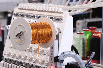 Leinwandbilder - A machine with a spool of wire on it. The wire is yellow and is being fed into the machine, sewing factory, clothing manufacturing