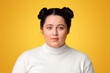 © Prostock-studio - Portrait of young plus size girl with double bun hairstyle standing over yellow background and looking at camera, free space
