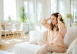 © Running opossum - Woman in pajamas sitting on a white sofa, enjoying a moment of relaxation while massaging her scalp
