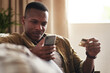 © Malambo/peopleimages.com - Black man, phone and online shopping with credit card on sofa for payment, banking or fintech at home. Young African, male person or shopper with debit on mobile smartphone for ecommerce at house