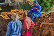 © poco_bw - african american plumber construction workers fixing a blocked drainage pipe in the trench outdoors