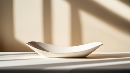 Poster - A curved abstract ceramic sculpture rests on a clean white surface, casting soft shadows against a sandy beige backdrop, ideal for showcasing lifestyle items