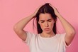 © miss irine - Young woman with long dark hair suffering from headache on pink background. She wears white t-shirt with loose hair waves, her face contorted in frown, eyes tightly shut, expressing pain, discomfort.