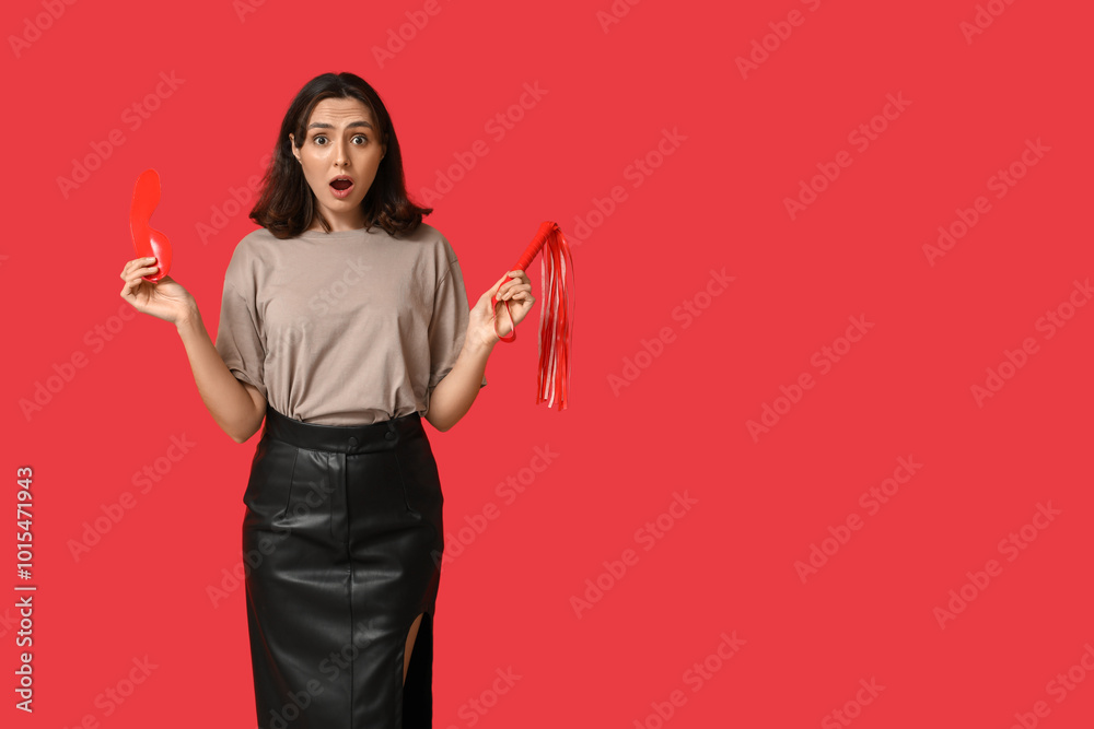 Shocked young woman with mask and whip on red background