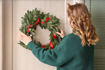 Poster - Woman in green sweater hanging Christmas mistletoe wreath on door