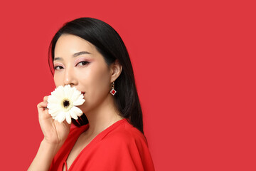 Poster - Beautiful young Asian woman with white gerbera flower on red background