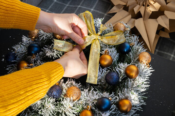 Woman tying decorative ribbon DIY process of woman making Christmas arrangement with decor of blue and yellow colors. Small business, self employed entrepreneur, self-made career. Series of handmade