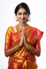 Young woman in vibrant red and gold saree stands confidently against white background. Gold jewelry, prayer position, colorful attire in focus. Simple background highlights woman beauty.