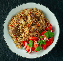 Delicious pilaf dish made with lamb, rice, and spices, accompanied by a refreshing tomato and onion salad with cilantro