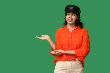 Wall Mural - Stylish African-American woman in hat showing something on green background