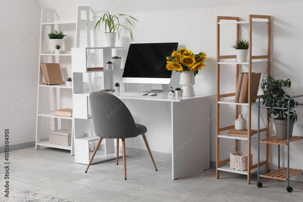 Modern workspace with computer and bouquet of sunflowers in light home office