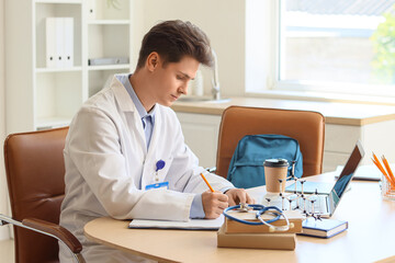 Canvas Print - Male medical intern writing at table in clinic