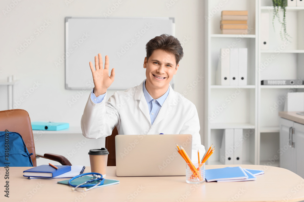 Male medical intern waving hand at table in clinic