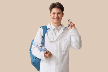 Canvas Print - Male medical intern with stethoscope and notebooks on beige background