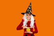 © be free - Halloween pumpkin in hand of teen girl wearing All Hallows party holiday costume of witch hat isolated on orange