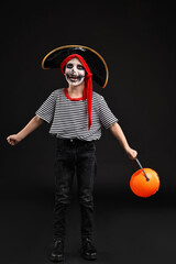 Wall Mural - Funny boy with pumpkin bucket dressed like pirate on black background. Halloween costume