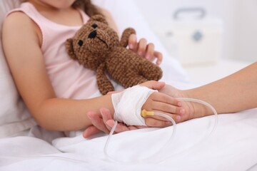 Canvas Print - Mother and her little daughter with IV drip on bed in hospital, closeup