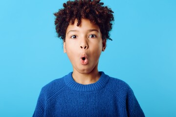young african american boy with a surprised expression against a blue background, capturing genuine 