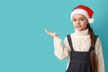 Canvas Print - Cute little girl in Santa hat showing something on blue background