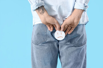 Wall Mural - Young man with hemorrhoids and sad smile on blue background, back view