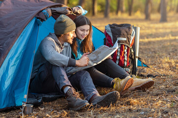 romantic couple camping in forest, sitting in tent during sunset, checking map, copy space