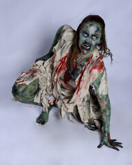 Canvas Print - portrait of scary female model wearing spooky halloween costume, ripped clothes and fake blood like an undead demon apocalyptic zombie character. Isolated figure, crawling poses dark studio background