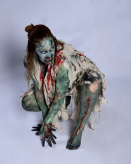 Canvas Print - portrait of scary female model wearing spooky halloween costume, ripped clothes and fake blood like an undead demon apocalyptic zombie character. Isolated figure, crawling poses dark studio background