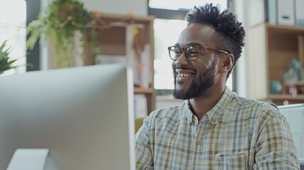Fototapete - A man with glasses and a beard is smiling at a computer monitor