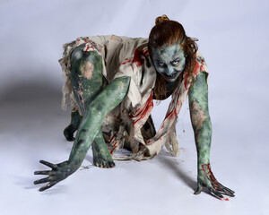 Canvas Print - portrait of scary female model wearing spooky halloween costume, ripped clothes and fake blood like an undead demon apocalyptic zombie character. Isolated figure, crawling poses dark studio background