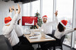 © sofiko14 - Successful team of multiethnic business people in Santa hats raising hands and screaming with happiness while working together in decorated with Christmas tree office in business center.