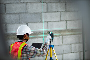 Construction worker is using cross-line laser level meter with line green beam to mark the floor in construction site. Tools for measuring distances.