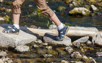 A young person is walking across a stream in a pair of blue shoes