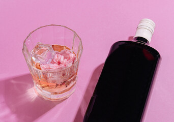 Two crystal glasses with rose cocktail and liquor bottle lying on pink background