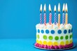 © volga - Colorful birthday cake with lit candles on blue background
