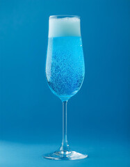 Carbonated drink in champagne glass on blue backdrop. Delicious alcoholic beverage.