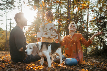 Young family with small children and dog on a walk in autumn forest. Throwing dry colorful leaves in the air.