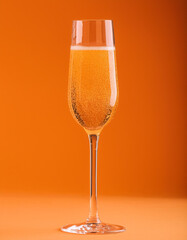 Carbonated drink in champagne glass on orange backdrop. Delicious alcoholic beverage.