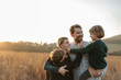© Halfpoint - Portrait of young family with two kids on a walk in autumn nature, standing in the middle meadow during sunset. Indian summer.