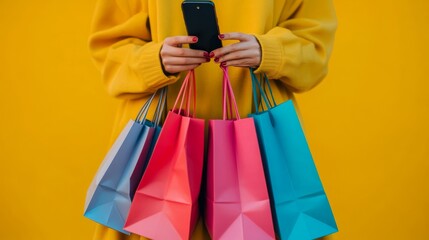 Wall Mural - a person holding a smartphone and colorful shopping bags against a bright yellow background.
