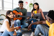 © Xavier Lorenzo - Young group of millennial people having fun together at modern flat. Happy indian man playing the guitar enjoying time with his friends at home