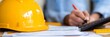 © Eva - Close-Up Of Yellow Hard Hat On Blueprint With Unrecognizable Person Taking Notes In The Background