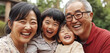 © kittikorn Ph. - A cheerful multigenerational family enjoying a joyful moment together outdoors. Grandparents and children smiling warmly, capturing the essence of family togetherness and happiness on a sunny day.