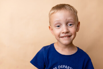 Smiling young boy in a blue shirt against a plain background, showcasing joy and innocence in a playful pose