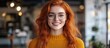 © GoDress - Portrait of a young woman with red hair wearing round glasses and a yellow sweater smiling at the camera.