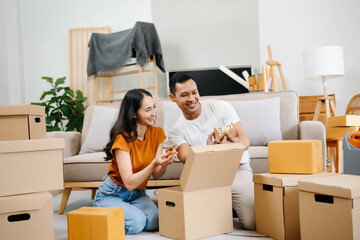 Asian young attractive couple man and woman use tablet and smartphone online shopping furniture decorate house with carton package move in new house. Young married asian moving home. .