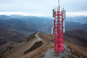 Red communication tower on a mountain ridge with antennas against a backdrop of expansive barren mountains. Cloudy sky over remote, rugged terrain.